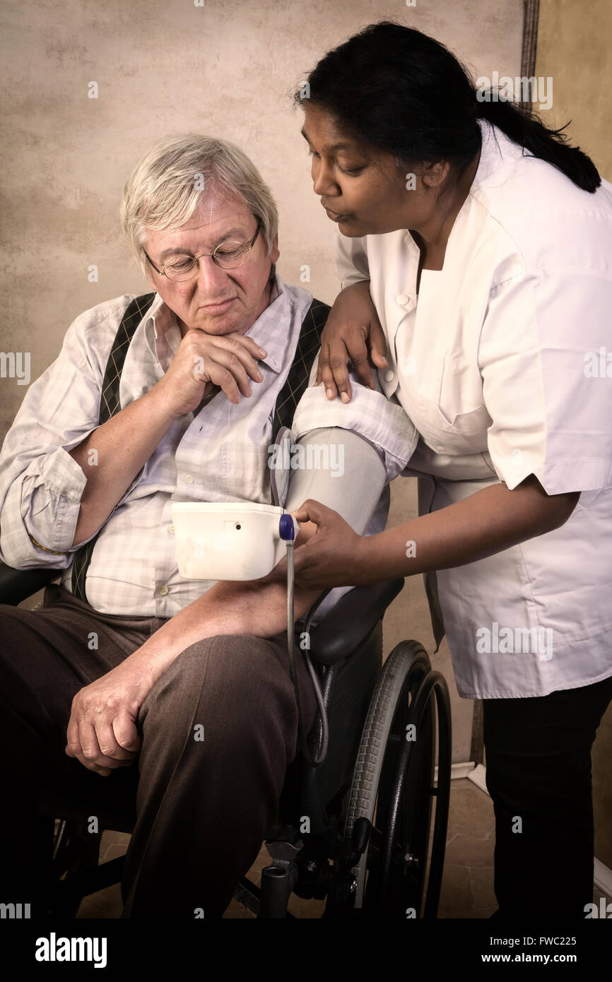 Krankenschwester, die Messung des Blutdrucks von einem älteren Mann im Rollstuhl Stockfoto