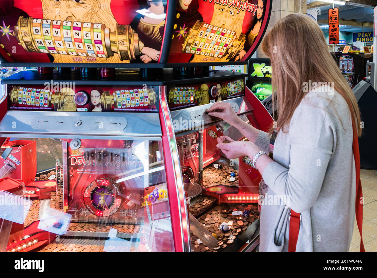 Eine Frau spielt eine 2P billiges Nudger Maschine in einer Kirmes in einem britischen Badeort. Stockfoto