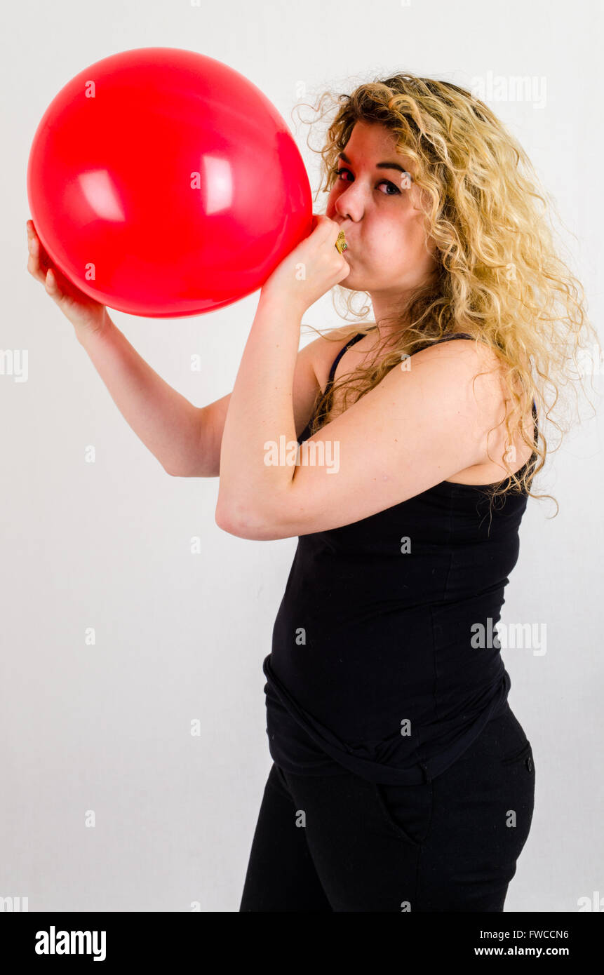 Einzelne Erwachsenfrau Sprengung ein Medium sized roten Ballon Stockfoto