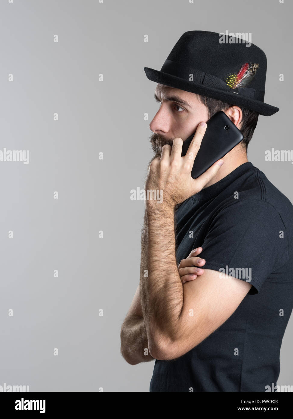 Seitenansicht des nachdenklichen bärtiger jungen Mann am Telefon wegsehen über graue Studio-Hintergrund Stockfoto