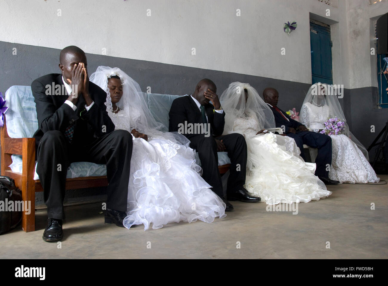 Lacekocot, Pader, Uganda. Freunde und Familie zu sammeln für die Gruppe Hochzeit von sechs Acholi Paare auf die Lacekocot IDP Camp.Three Bräute und Bräutigame sitzen und beten Stockfoto