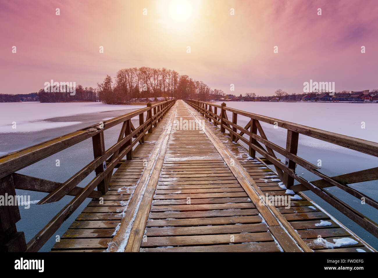 Perspektivische Ansicht der Holzbrücke über den zugefrorenen Fluss im Abendlicht. Trakai Stadt, Litauen Stockfoto