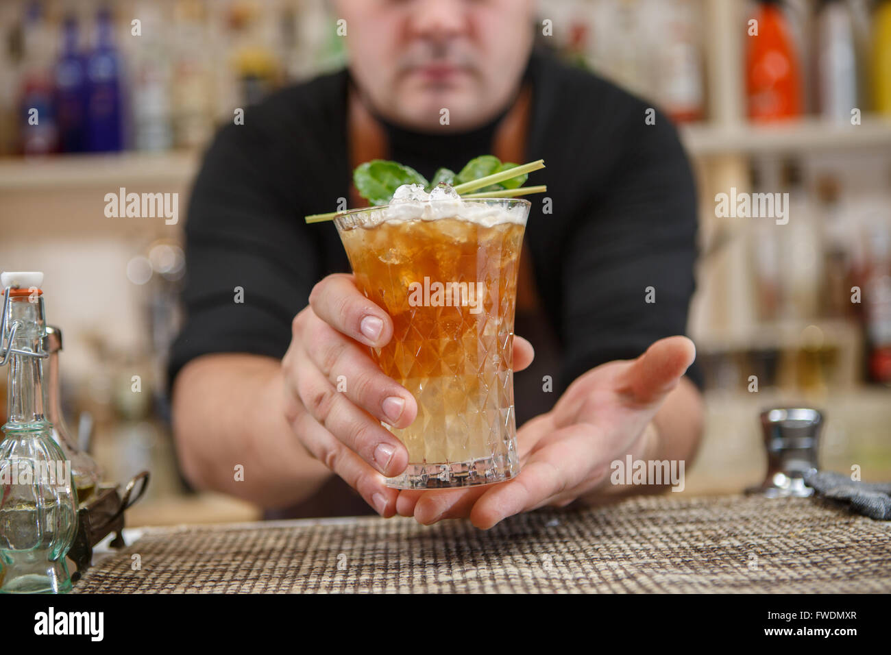 Barkeeper steht in Pubб mit cocktail und geben Glas nach vorne. Getränke im Mittelpunkt. Stockfoto