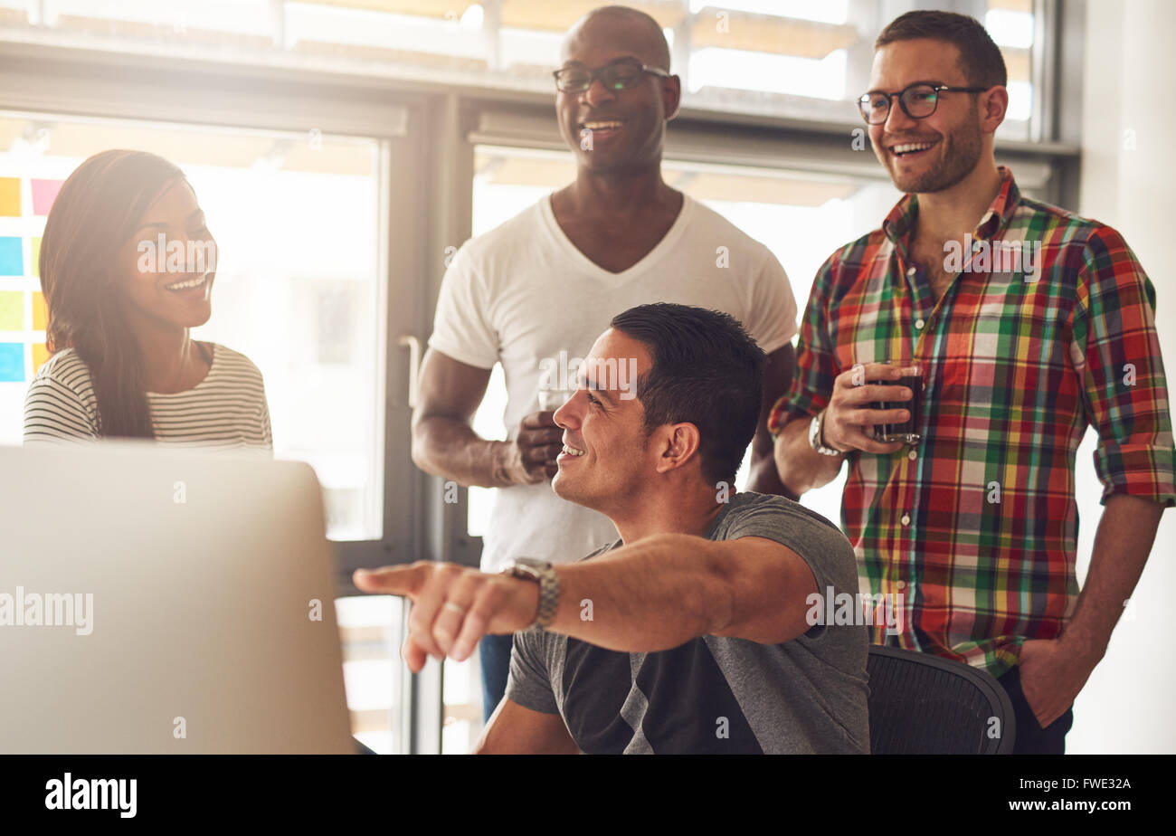 Hübscher junger Erwachsener zeigen etwas auf seinem Computer zu einer Gruppe von drei männlichen und weiblichen lässig gekleidet Freunde halten drin Stockfoto