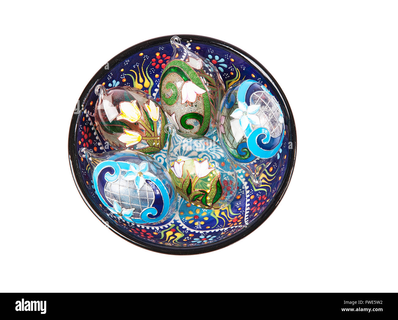 Bunte Zusammensetzung von fünf ornamentalen Eiern aus Glas, die in einer tiefen Blau gemusterten Keramik Kappe sind. Ansicht von oben. Isoliert Stockfoto