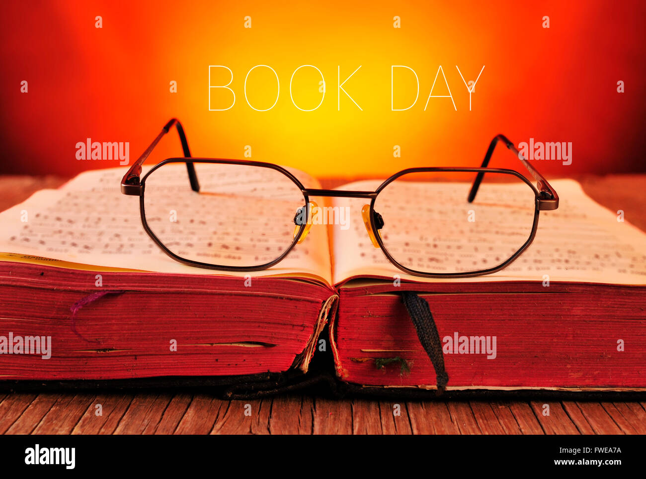 ein paar Brillen auf ein offenes alte Buch platziert auf einem rustikalen Holztisch und Tag der Text des Buches verblasst im Hintergrund Stockfoto
