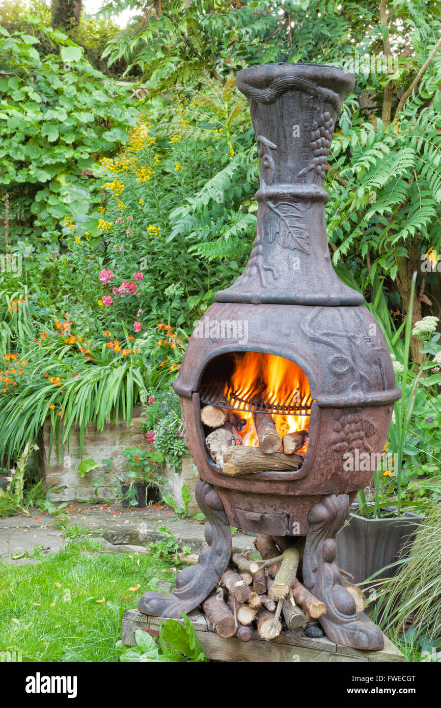 Rustikale gusseiserne Holzofen, mexikanische Chiminea mit Flammen, bereit zum Grillen, im Sommer Landhaus Blumengarten Stockfoto