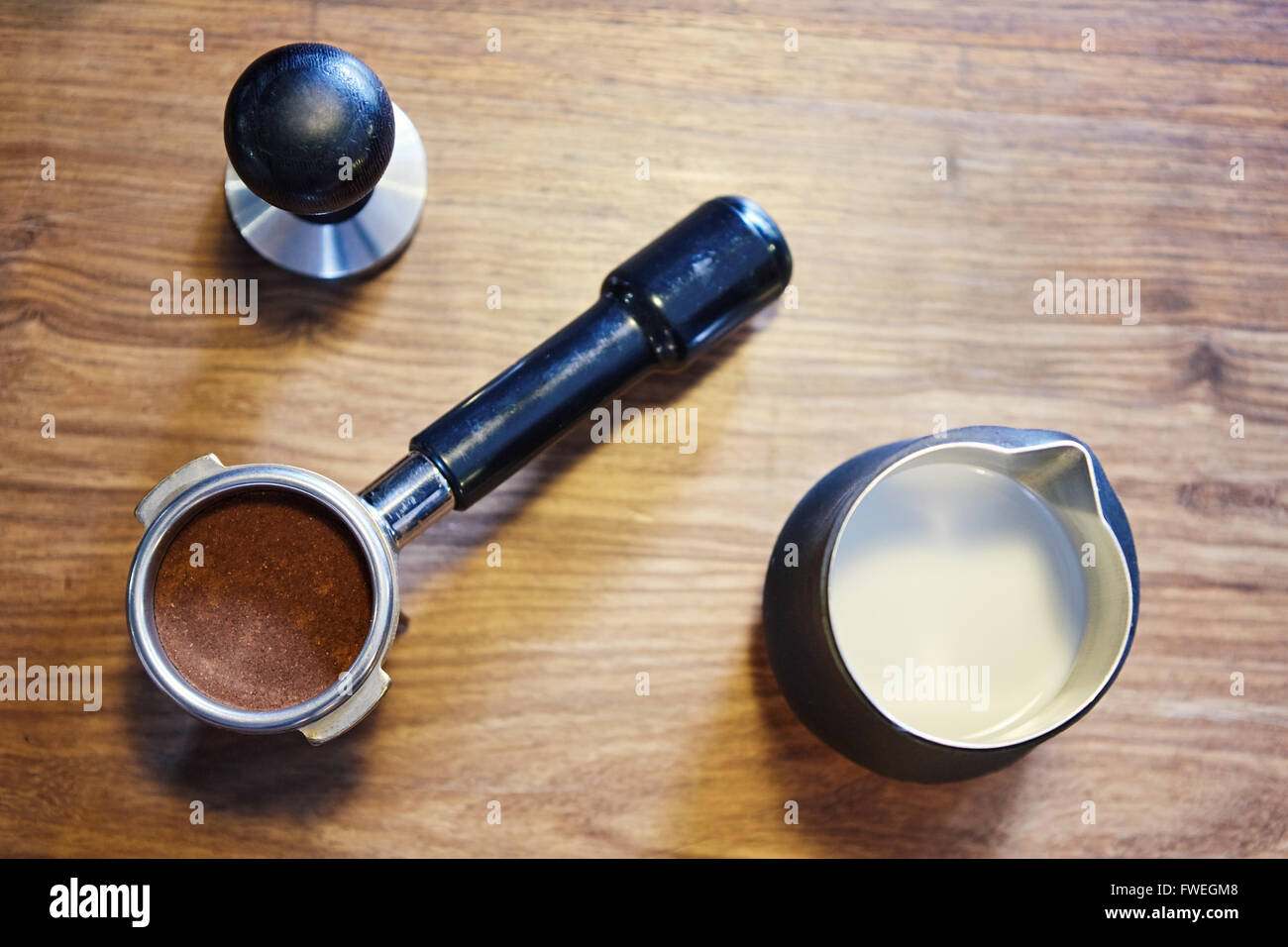 Obenliegende Bild von einem Edelstahl-Krug mit Milch drin, eine glänzende neue Siebträger mit frisch gemahlenem Kaffee und ein Metall tamp Stockfoto
