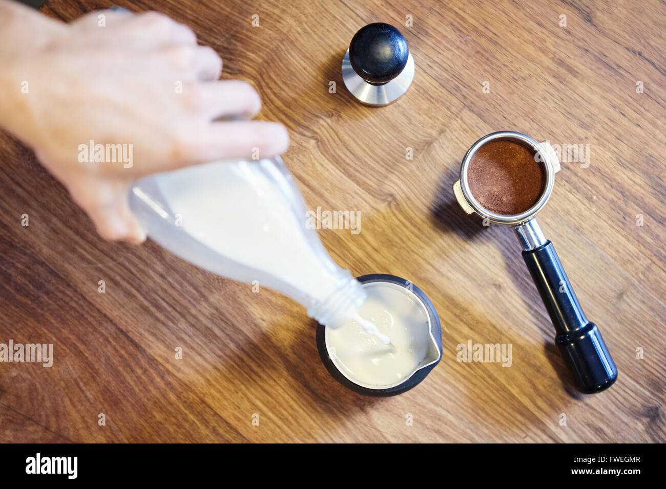 Eine Hand hält eine Flasche Milch und gießen es in ein Metall Kanne mit einem Siebträger mit frisch Boden c Overhead Schuss Stockfoto