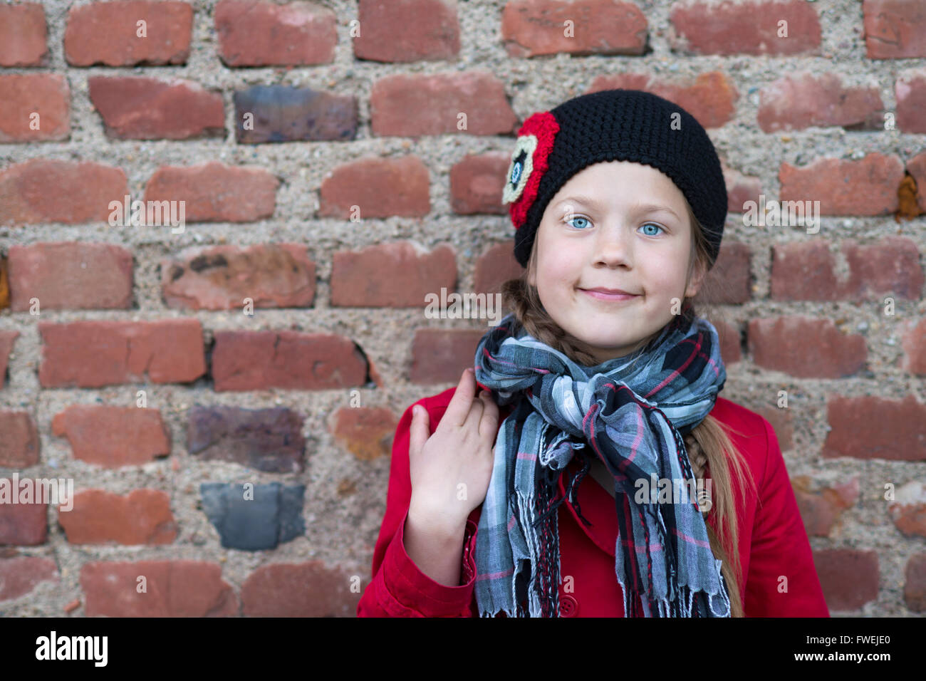 ehrliches Porträt von Mädchen im roten Mantel in der Nähe der alten roten Backsteinmauer Stockfoto