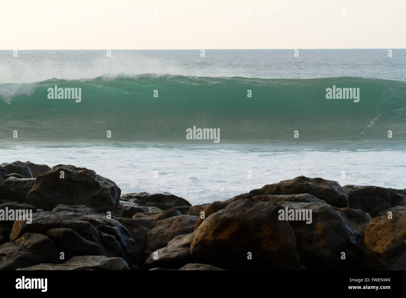 Diese riesige Welle bricht gleich hinter einigen Felsen in der Nähe von Pipeline auf der Nordküste von Oahu in Hawaii bei einem großen Sturm. Stockfoto