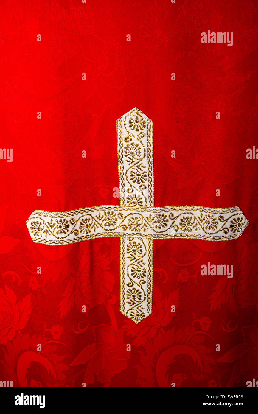 Ein gold und weißem Kreuz wird auf ein rotes Gewand genäht, die ein Priester trägt. Stockfoto