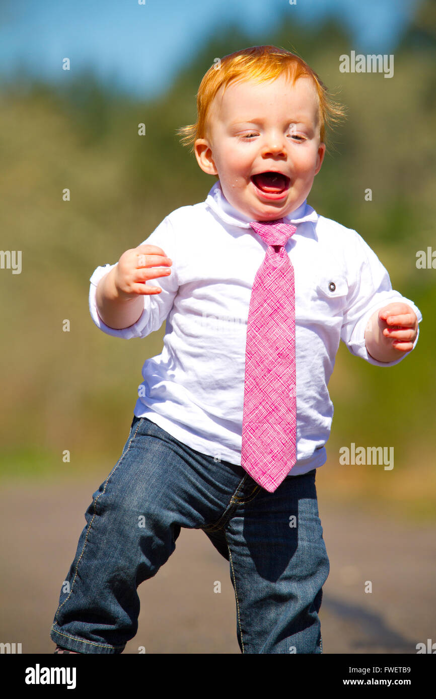 Ein einjähriger Junge dabei einige der seine ersten Schritte im Freien auf einem Pfad mit selektiven Fokus während des Tragens ein schönes Hemd und eine neckt Stockfoto