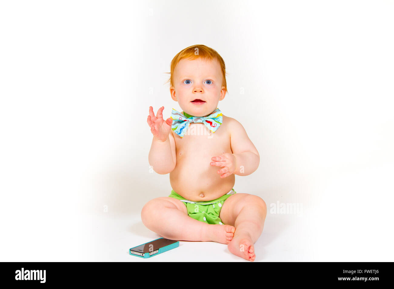 Ein einjähriger Junge spielt mit einem Handy im Studio mit einem weißen Hintergrund. Stockfoto