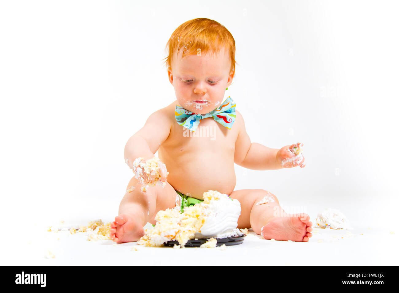 Ein Baby bekommt, Kuchen zum ersten Mal an seinem ersten Geburtstag in diesem Kuchen smash im Studio vor einem weißen Hintergrund zu essen. Stockfoto