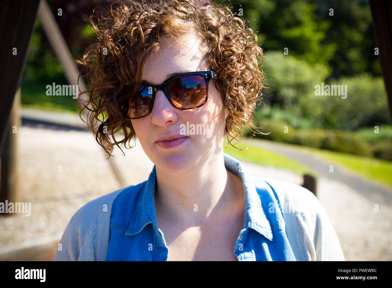 Diese schöne, attraktive Frau trägt Sonnenbrille im Freien in einem Park für ein einfaches Porträt einer weiblichen Person. Stockfoto