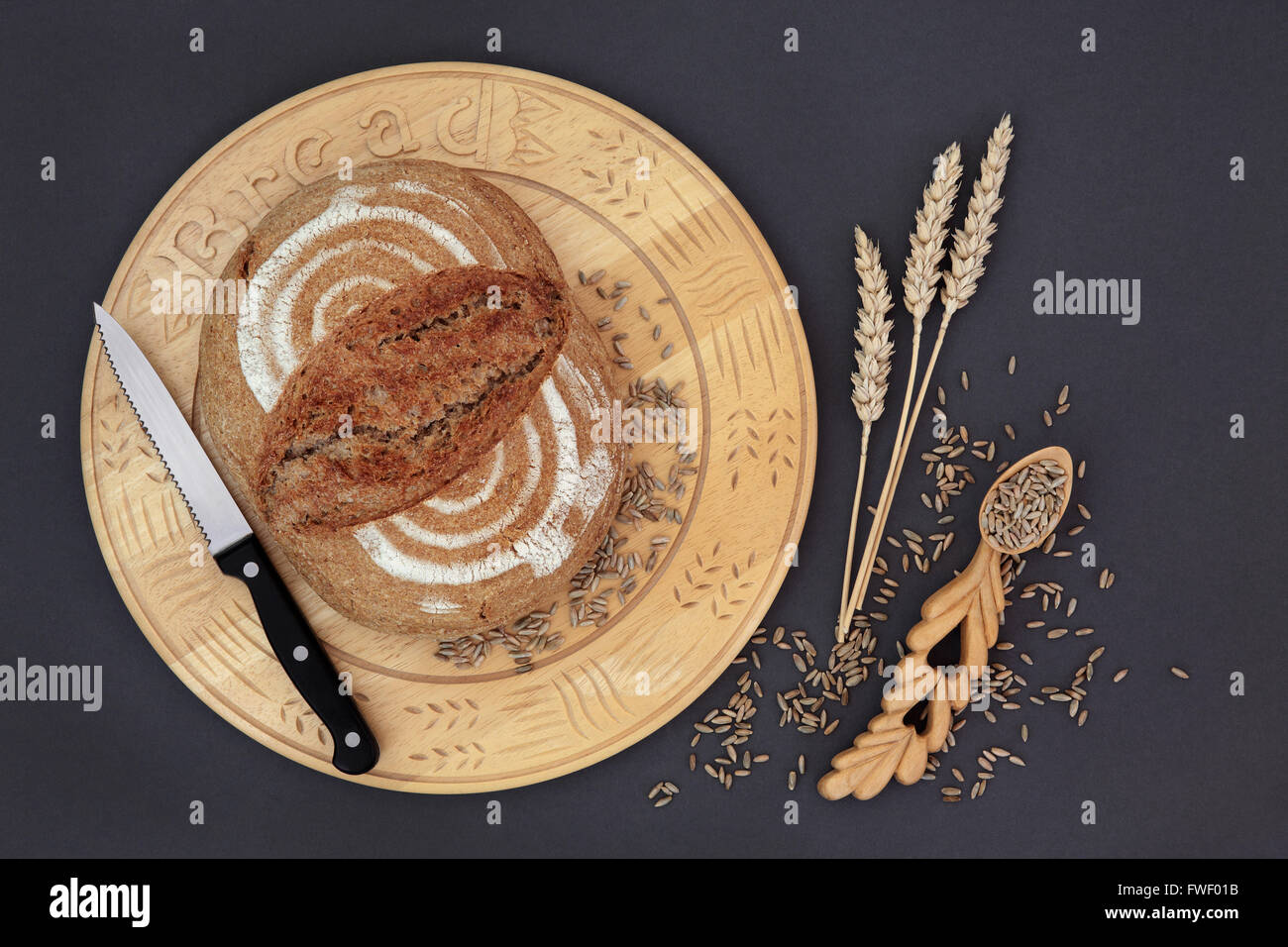 Hausgemachtes Roggenbrot Brot auf einem Holzbrett mit Messer, Korn und Weizen scheiden mit geschnitzten Liebe Löffel auf grauem Hintergrund. Stockfoto