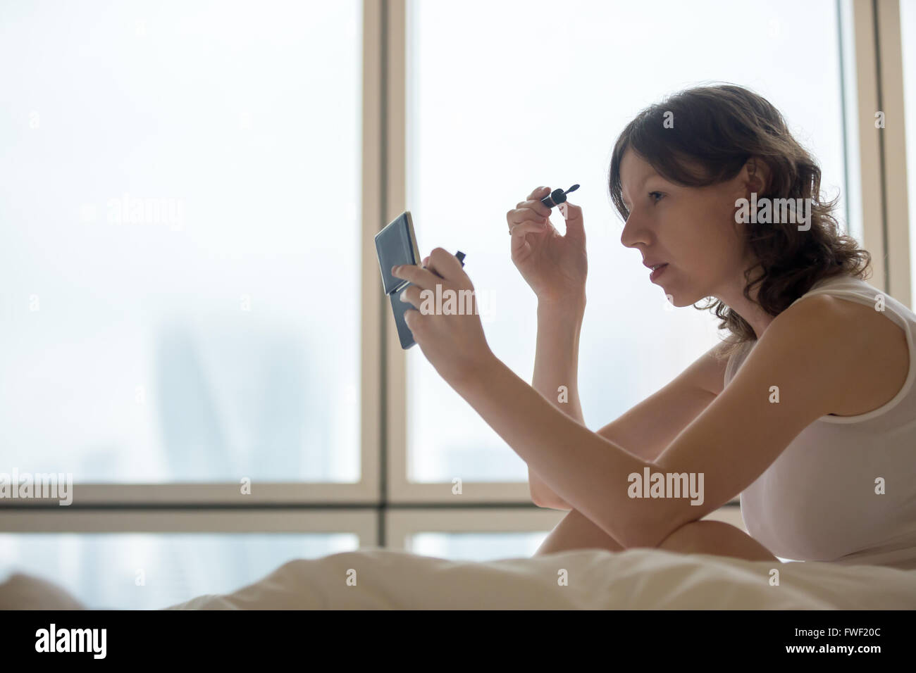 Lifestyle Portrait junge Frau sitzt auf dem Bett und setzen auf Mascara nach dem Aufstehen. Kaukasische weibliches model Stockfoto