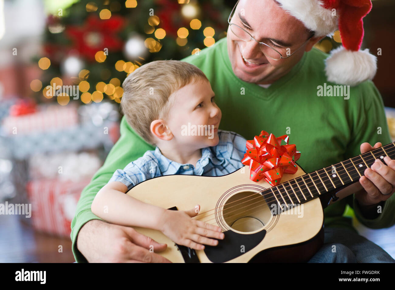 Vater und Sohn sitzen durch einen Weihnachtsbaum, eine Gitarre zu spielen. Stockfoto