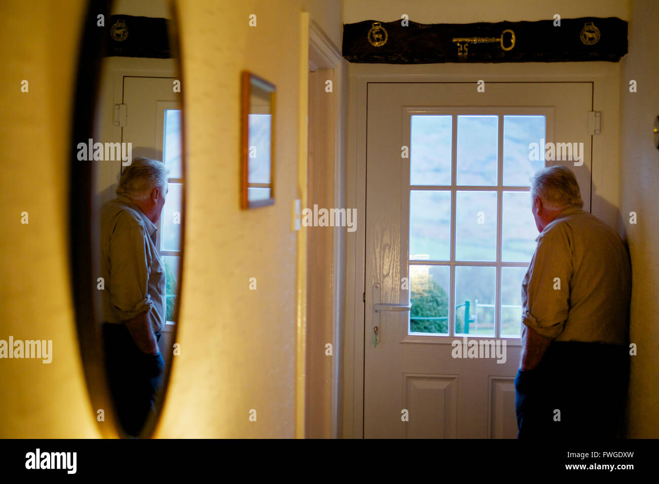 Ein älterer Mann stand durch eine Tür mit Blick durch die Fensterscheiben. Stockfoto