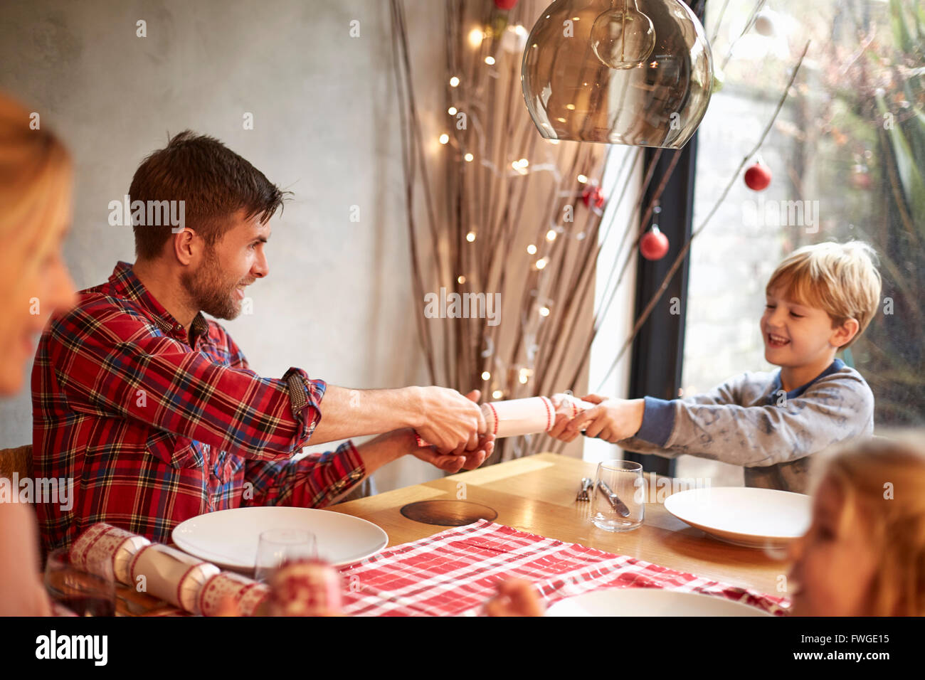 Eine Familie von vier Personen, zwei Erwachsene und zwei Kinder sitzen um einen Tisch in der Weihnachtszeit, Cracker ziehen. Stockfoto