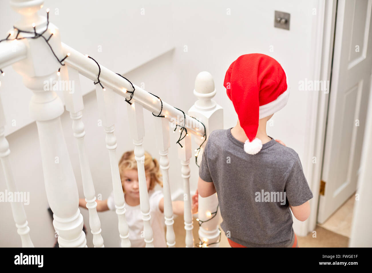 Ein Junge und ein Mädchen stürzte die Treppe hinunter am Weihnachtsmorgen, man trägt eine Weihnachtsmütze. Stockfoto