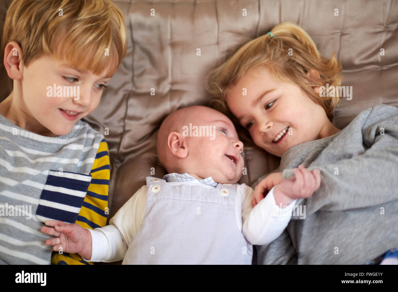 Drei Kinder auf einem Bett, einem jungen und Mädchen mit einem Baby zwischen ihnen liegen. Stockfoto
