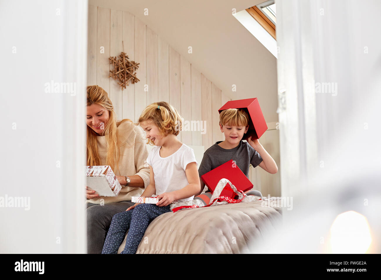 Weihnachtsmorgen in einem Einfamilienhaus. Eine Mutter und zwei Kinder sitzen auf einem Bett Eröffnung präsentiert. Stockfoto