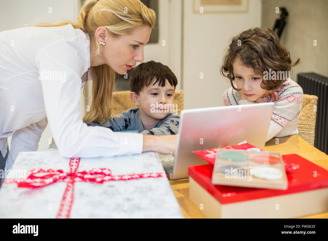 Zwei Kinder und ihre Mutter Blick auf einem Laptop-Computer-Bildschirm ein Küchentisch. Stockfoto