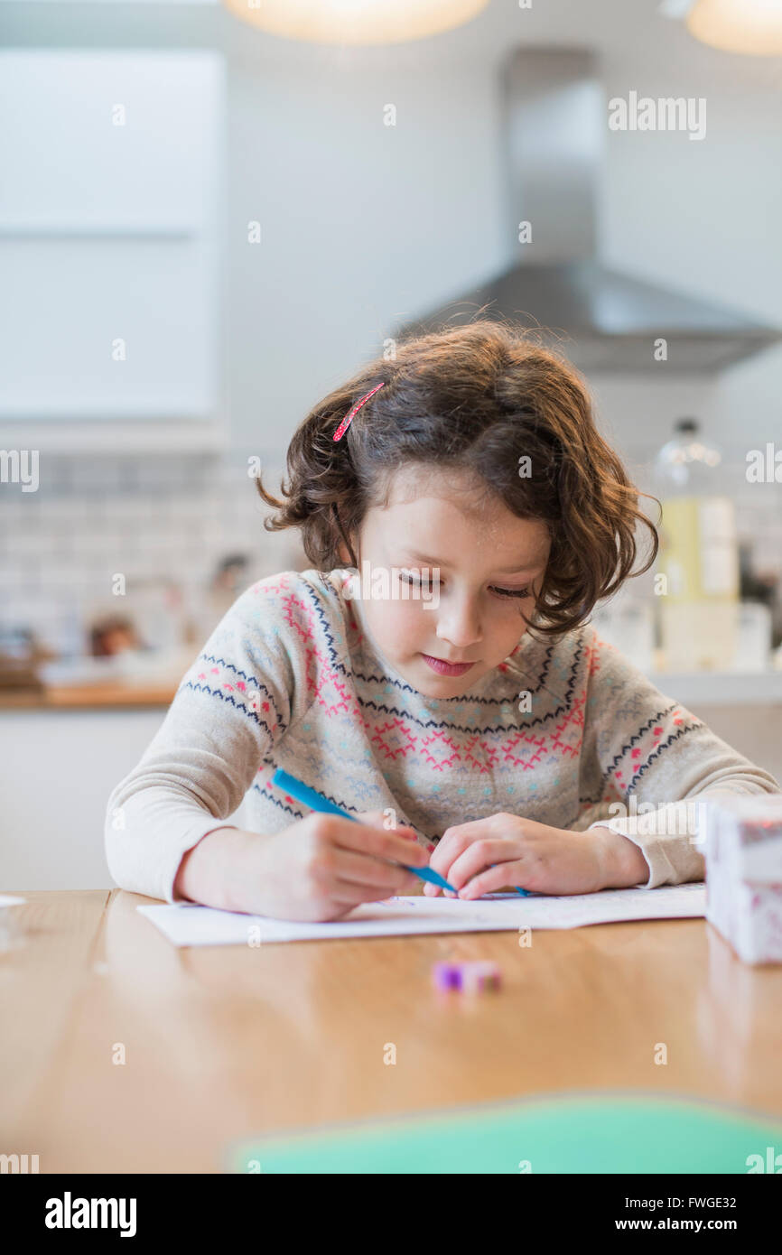 Ein Mädchen sitzt an einem Küchentisch, eine Karte oder ein Brief zu schreiben. Stockfoto