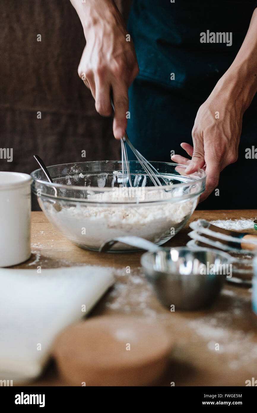 Eine Person mit einem Schneebesen mischen Zutaten in einer Schüssel auf einem Küchentisch. Stockfoto