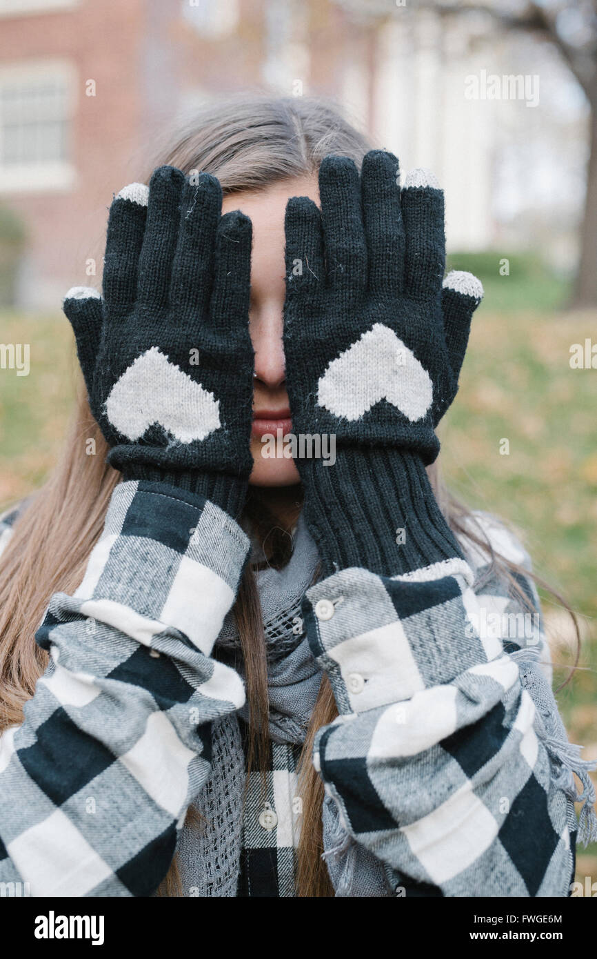 Ein Mädchen mit wolligen Handschuhen mit einem herzförmigen Design, versteckt ihr Gesicht. Stockfoto