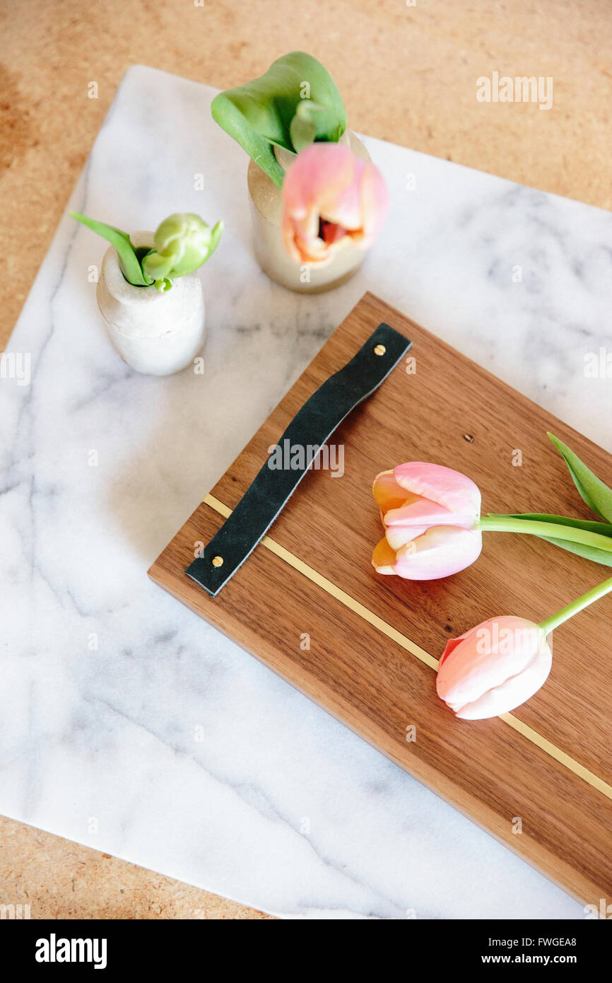 Eine Marmorplatte mit zwei Vasen und rosa Tulpen und ein Holzbrett mit Griff. Stockfoto