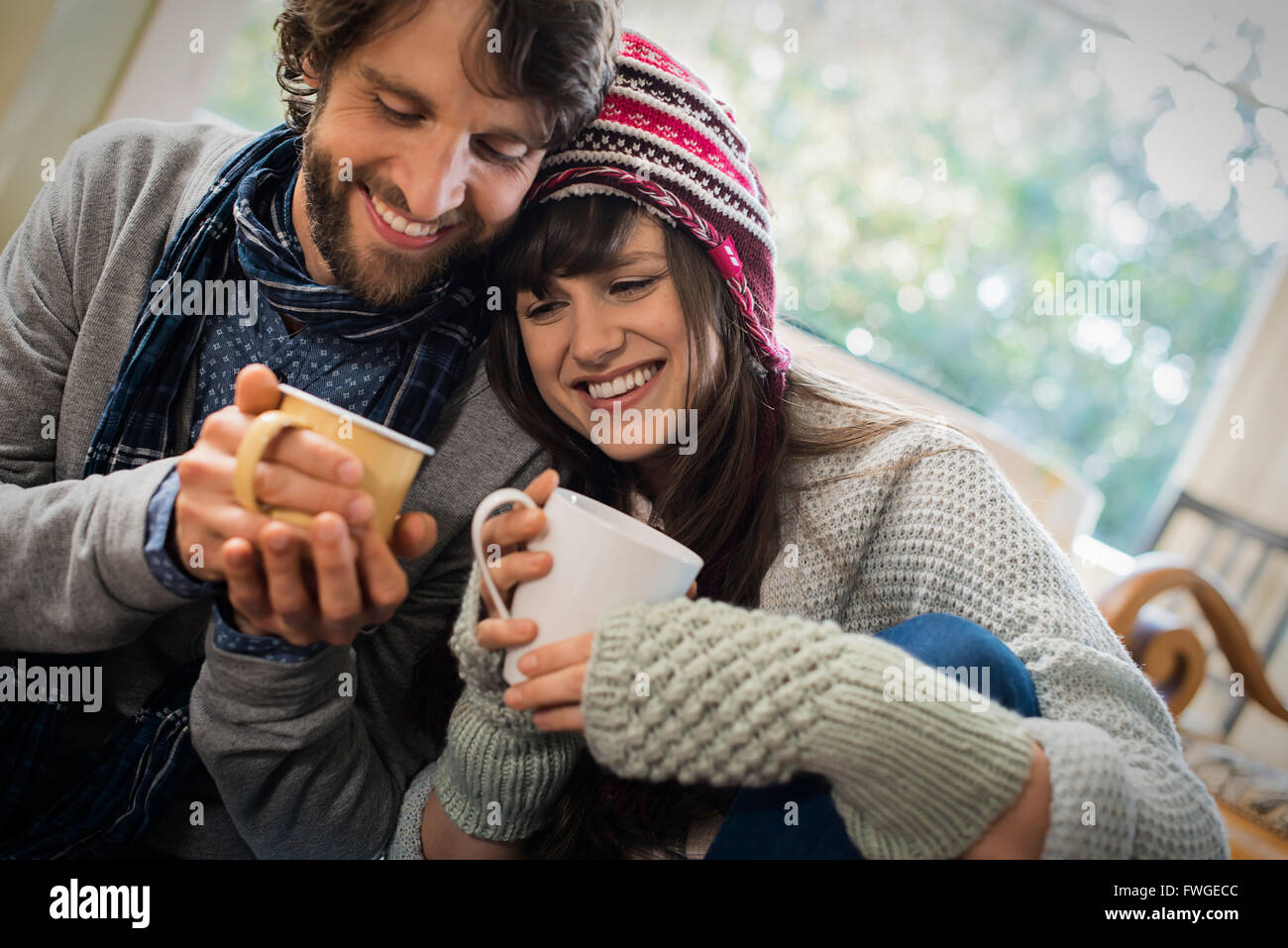 Ein paar, Mann und Frau sitzen dicht beieinander mit ihren Händen um Tassen Aufwärmen. Stockfoto