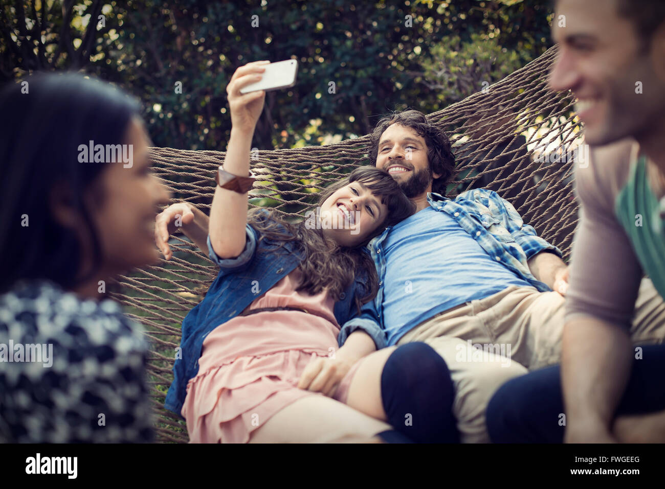Eine Gruppe von Freunden Faulenzen in einer großen Hängematte im Garten ein Bier, und ein Selbstporträt. Stockfoto