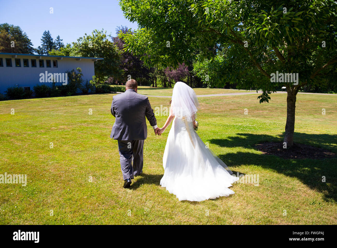 Eine Braut und Bräutigam zu Fuß entfernt von der Kamera Hand in Hand an diesem Veranstaltungsort Hochzeit im Freien in einem Park nach nur binden die Stockfoto