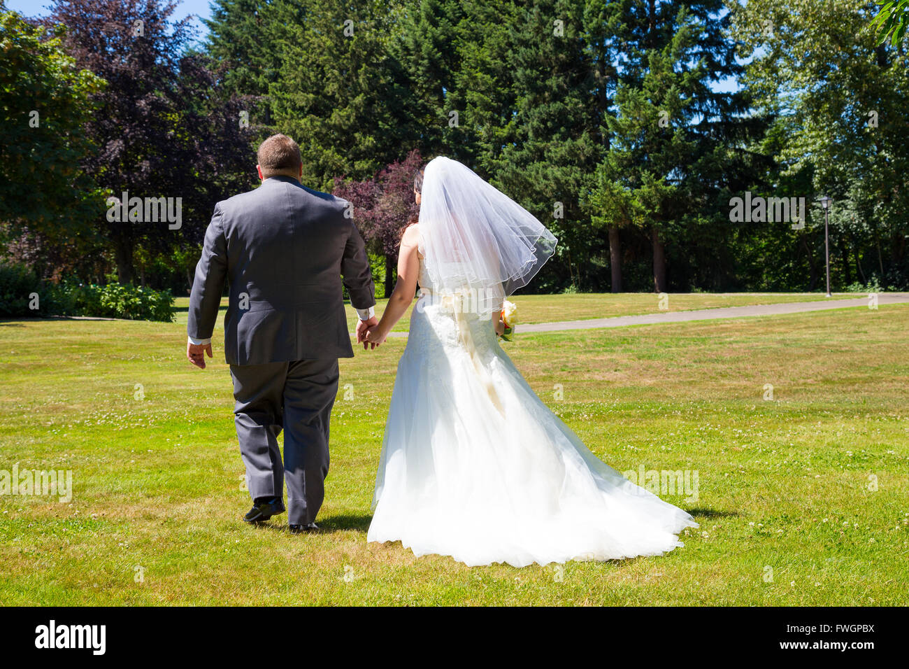 Eine Braut und Bräutigam zu Fuß entfernt von der Kamera Hand in Hand an diesem Veranstaltungsort Hochzeit im Freien in einem Park nach nur binden die Stockfoto