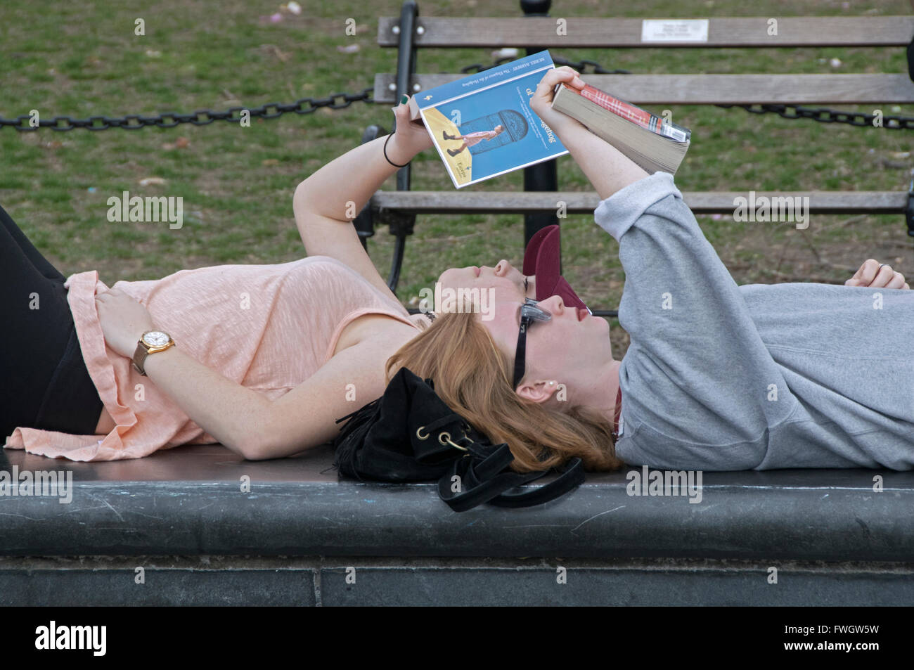 Zwei junge Damen lesen liegend auf einer konkreten Bank im Washington Square Park in Greenwich Village in New York City. Stockfoto