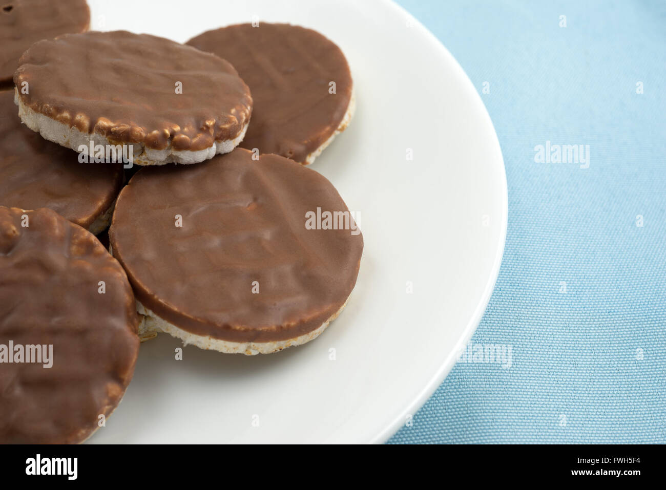 Enge Seitenansicht einer Gruppe von Bio-Reis Kekse mit Milchschokolade Sahnehäubchen auf einem weißen Teller oben auf einer blauen Tischdecke. Stockfoto