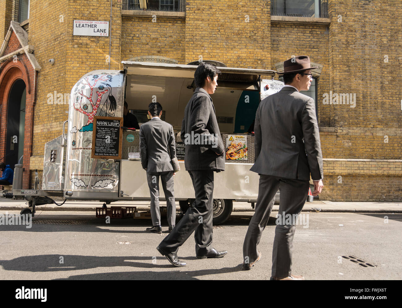 Eine elegant gekleidete Chinesischer Mann kauft eine Naan springen von einem glänzenden Revival Trailer street Verkäufer auf Leder Lane in London, UK. Stockfoto