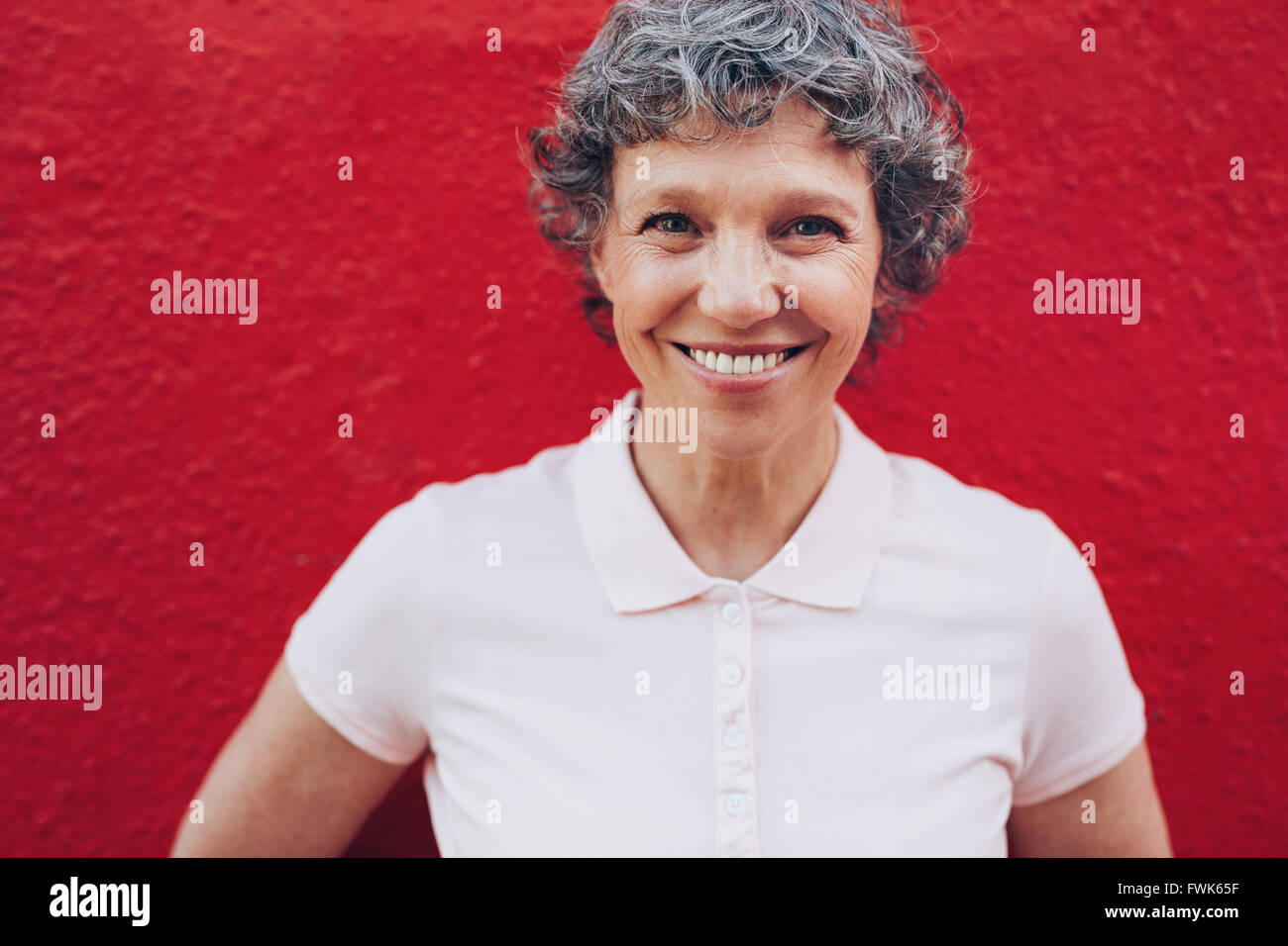 Porträt des Lächelns Reife Frau vor rotem Hintergrund hautnah. Applying Frau mit schönen Lächeln. Stockfoto