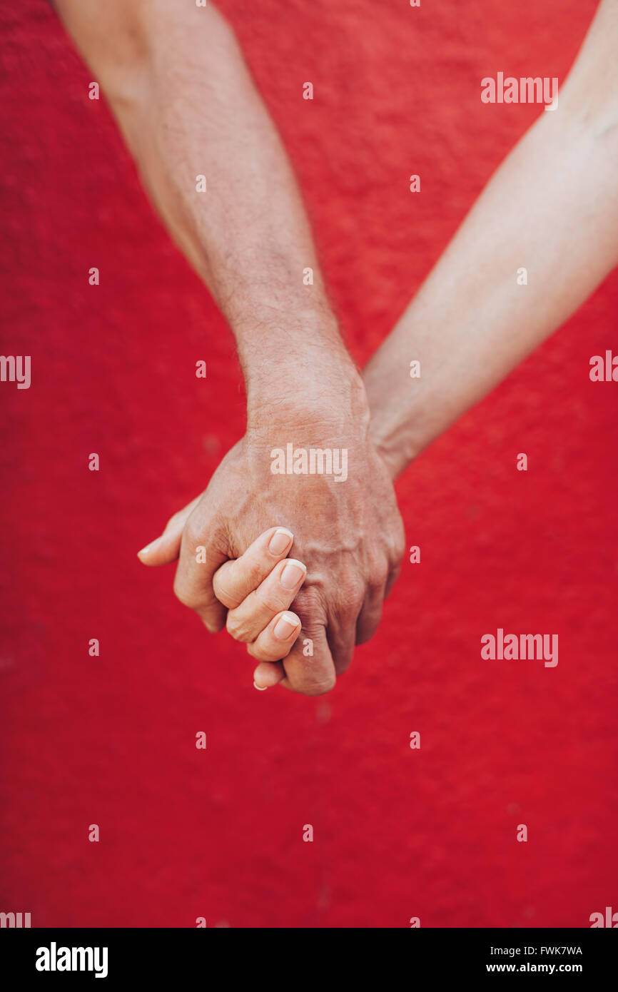 Nahaufnahme des reifes Paar Hand in Hand gegen die rote Wand. Vertikale Aufnahme des liebenden Mann und Frau, die Hand in Hand. Stockfoto