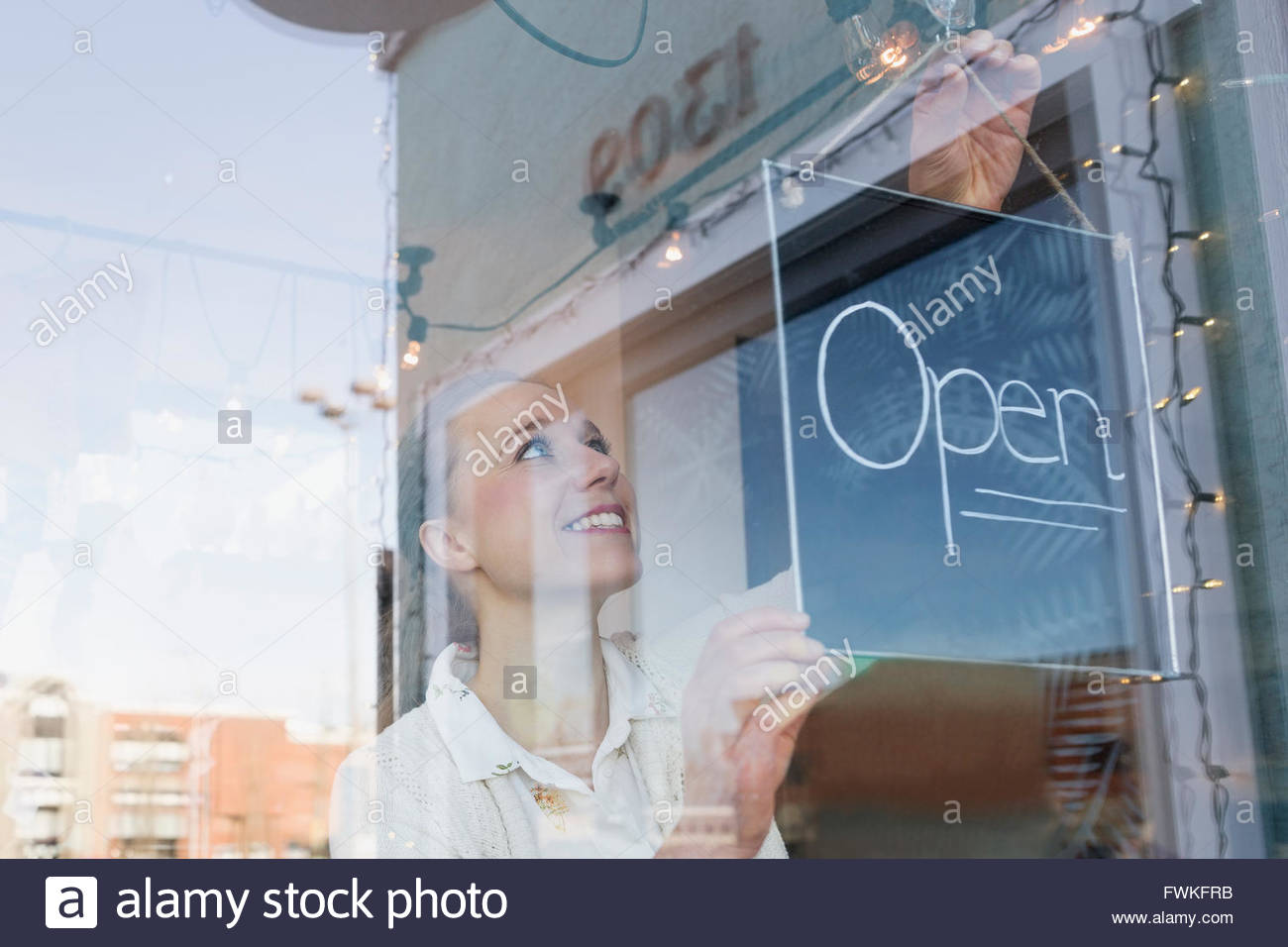 Lächelnde Ladenbesitzer Schild "geöffnet" am Fenster drehen Stockfoto