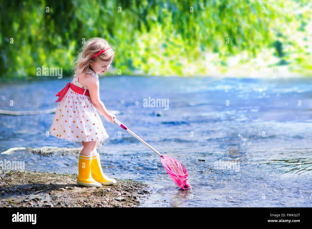 Kind spielt in einem Fluss. Niedliche kleine Mädchen in einem Sommerkleid  und Regen Stiefel fangen Fisch und Frosch mit einem bunten net stehen  Stockfotografie - Alamy