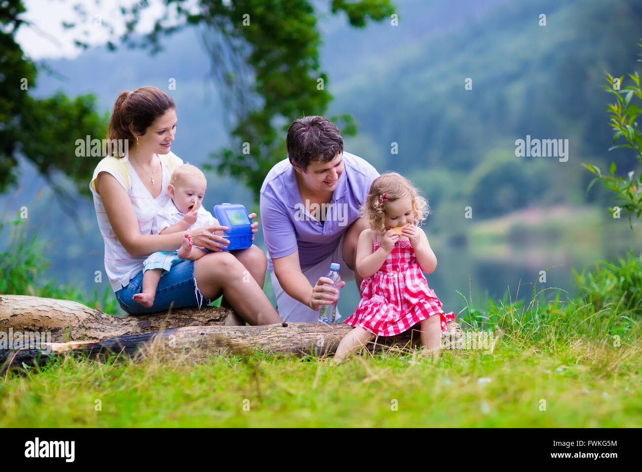 Familie auf Sommerwanderung. Junge Eltern mit Kindern wandern an einem See. Mutter, Vater und zwei Kinder haben Picknick im freien Stockfoto