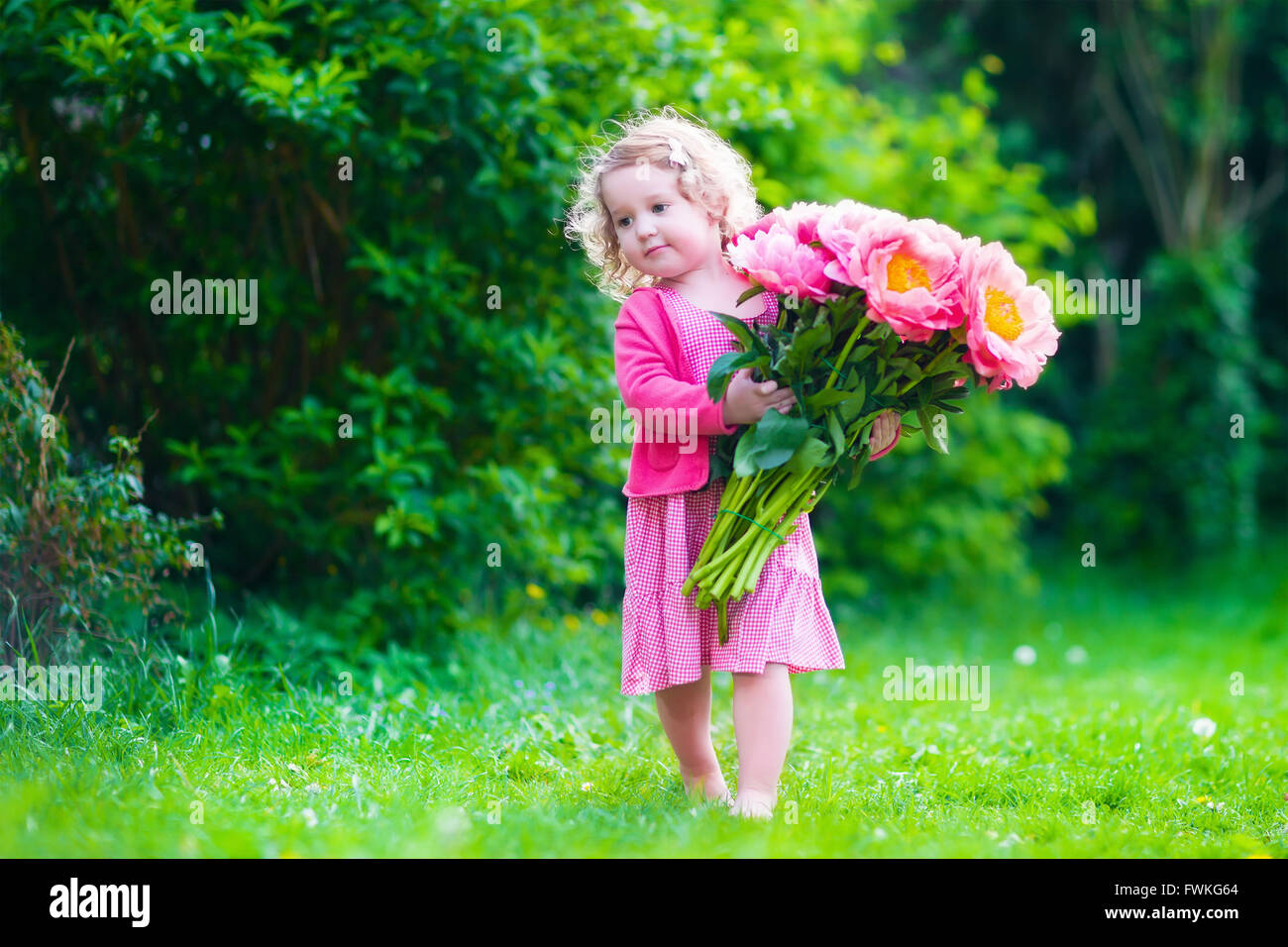 Kleine süße Mädchen mit Pfingstrosen Blumen. Das Kind trägt ein rosa Kleid im Sommergarten spielen. Kinder im Garten. Kinder spielen im freien Stockfoto