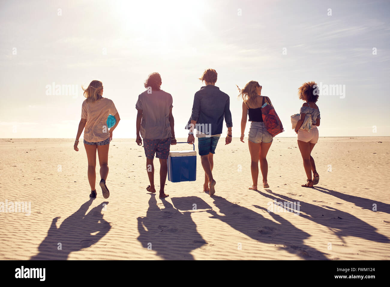 Hintere Ansicht Portrait Gruppe von jungen Leuten am Strand tragen eine Kühlbox. Junge Männer und Frauen am Meeresufer. Freund Stockfoto
