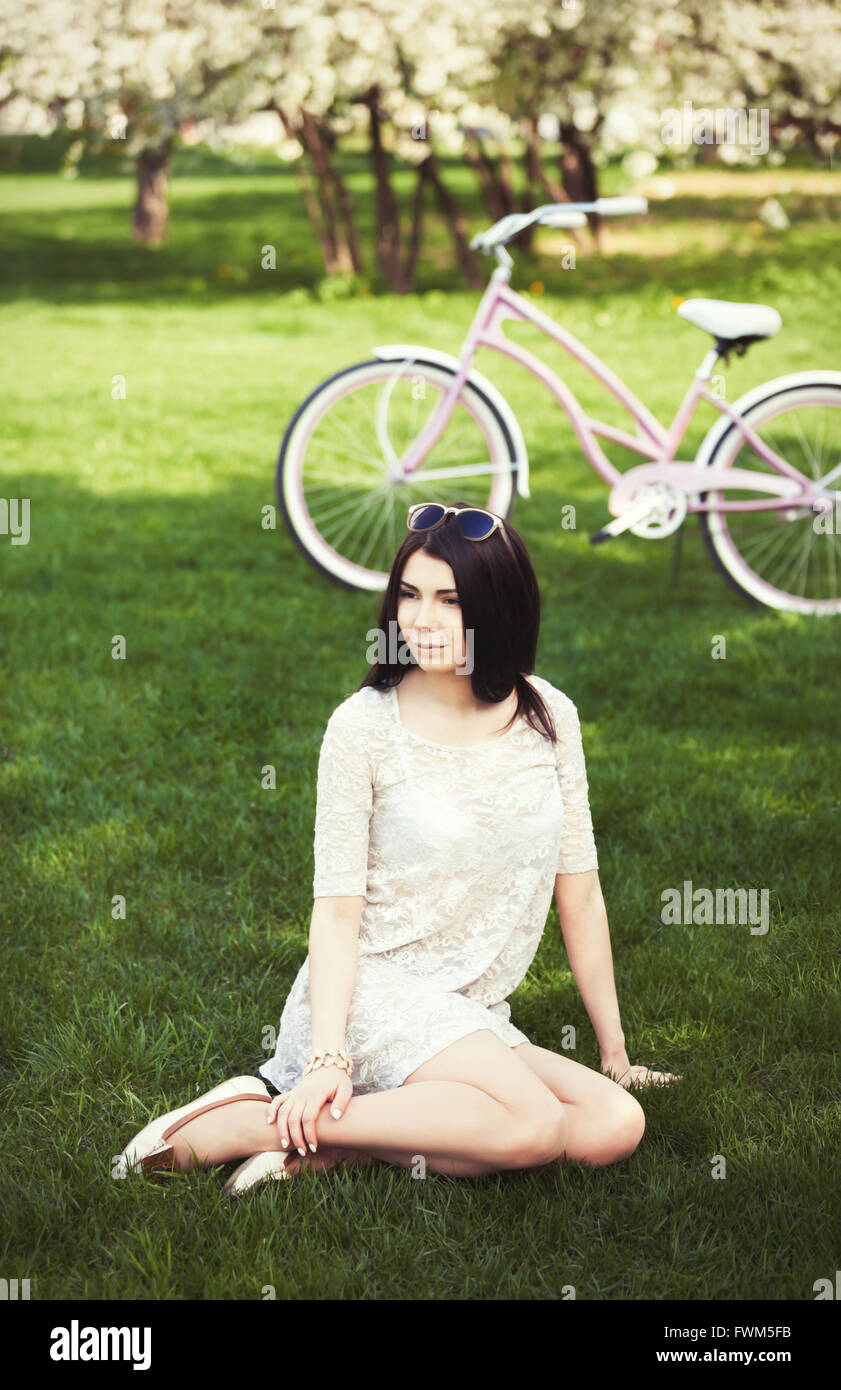 Attraktive junge Mädchen mit rosa Fahrrad Freizeitgestaltung im grünen Park am hellen Sommer oder Frühling. Model trägt ein Sommerkleid und Sonnenbrillen, ihre Stimmung ist toll und sie ist schön Stockfoto