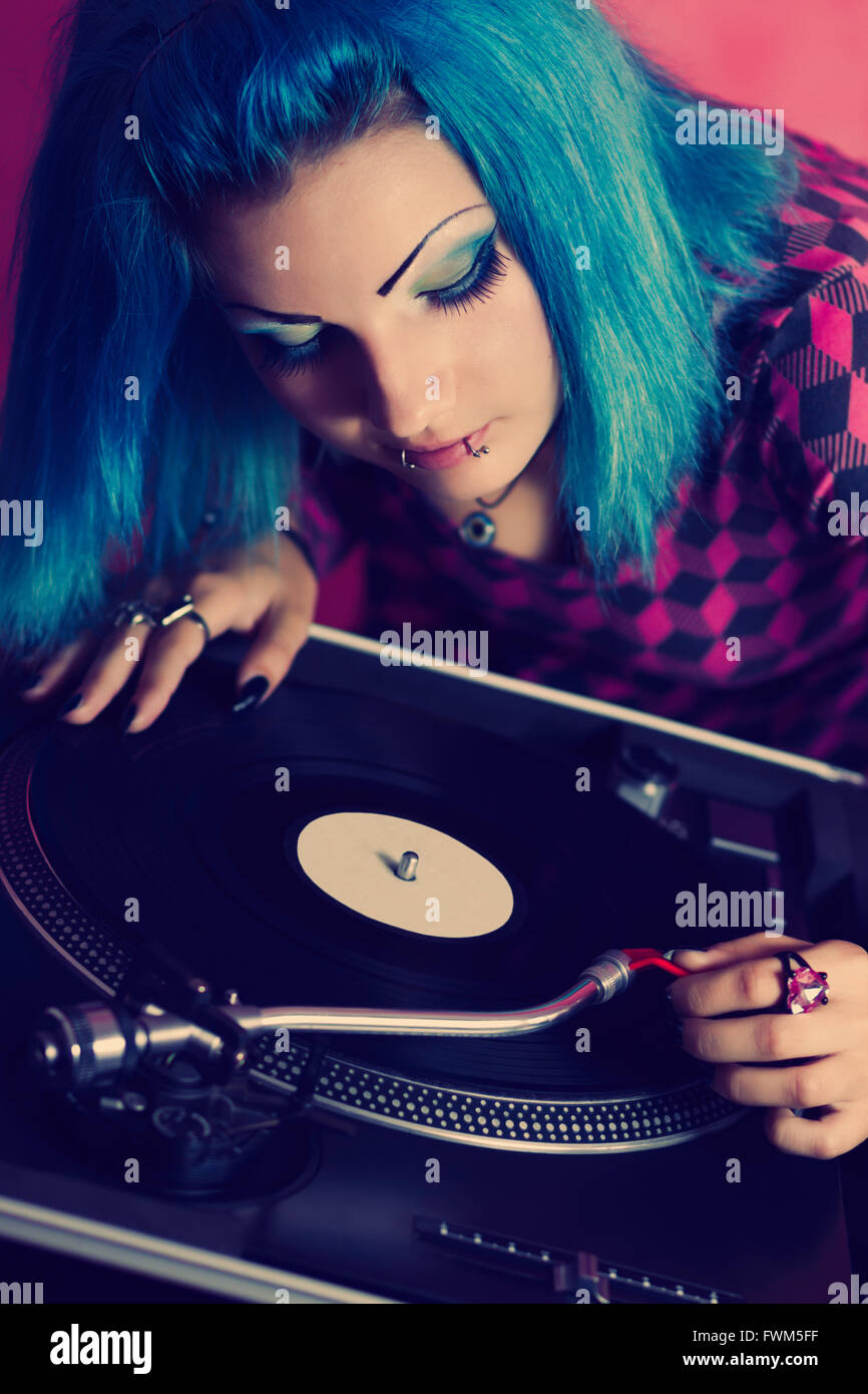 Stilvolles junge Mädchen DJ mit blau gefärbten Haaren setzen eine Nadel auf einen Datensatz mit Musik. Professioneller Plattenspieler Ausstattung für einen DJ, Diskothek und audio-Enthusiasten Stockfoto