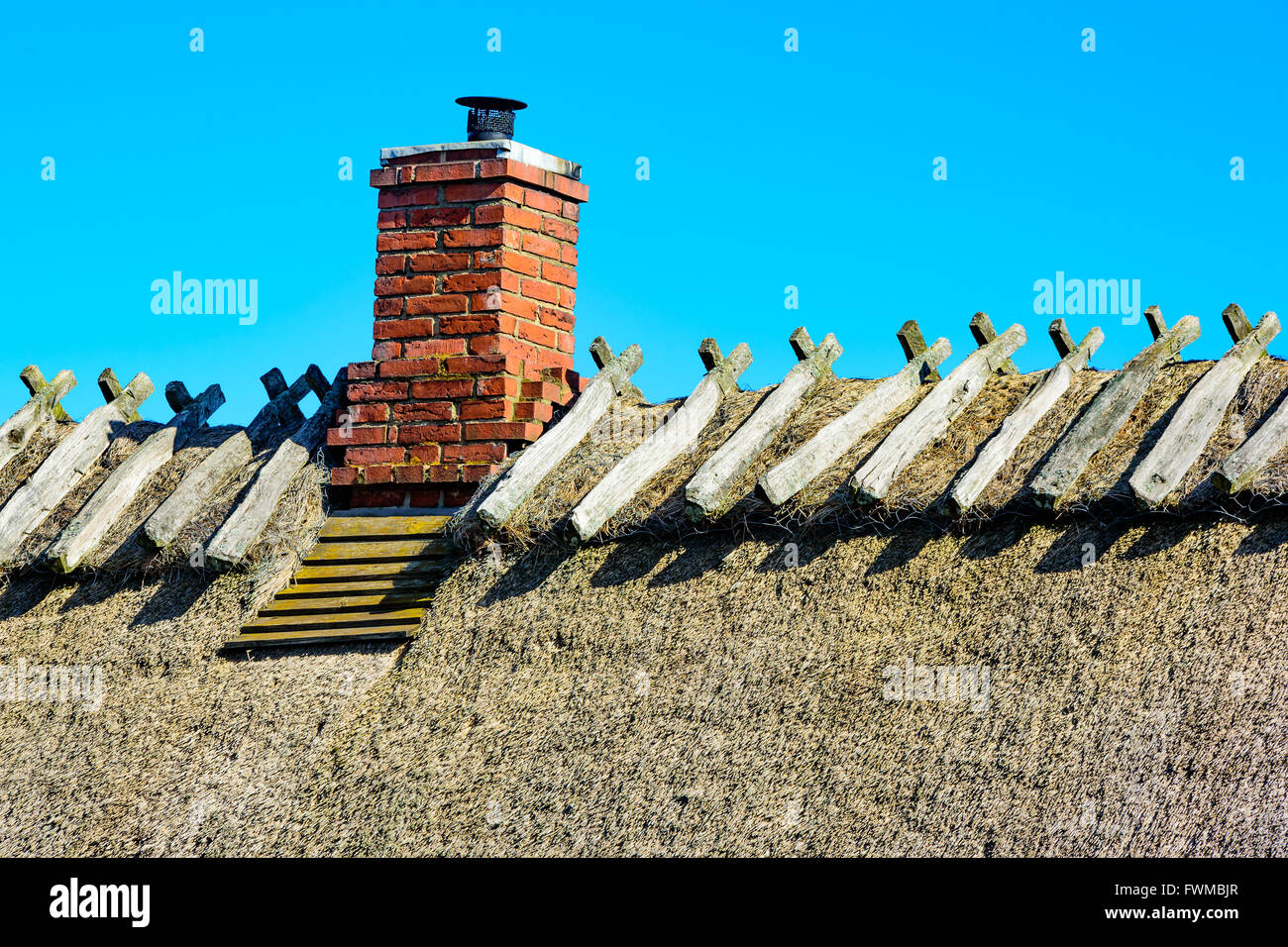 Stroh auf dem Dach mit einem alten Kamin vor einem blauen Himmel. Stockfoto